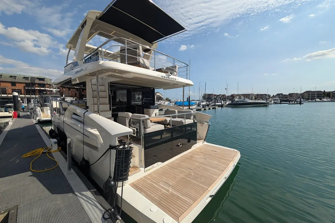 A luxury motor yacht docked at a marina, showcasing a spacious deck, stylish seating, and nearby boats under a clear sky.